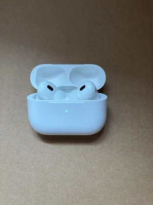 Apple AirPods Pro med laddningsetui - Säljer ett par vita Apple AirPods Pro med trådlöst laddningsetui. Hörlurarna har en stilren och kompakt design med silikonproppar för bra passform. Perfekta för musik, samtal och träning. Laddningsetuiet är också vitt och har en LED-indikator på framsidan.