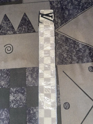 Två rutiga bälten i beige och vitt - Säljer två snygga bälten med rutigt mönster. Ett bälte i beige med röda och svarta rutor och ett i vitt och grått med metallspänne. Perfekta accessoarer för att lyfta din outfit.