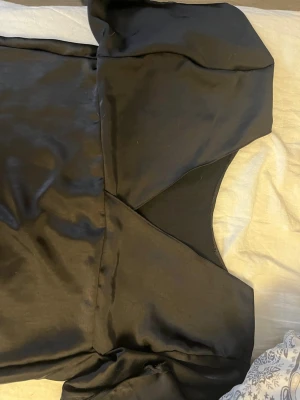 Svart satin blus med kort ärm - Elegant svart blus i glansigt satinmaterial med korta ärmar och v-ringad hals. Blusen har en stilren design och mjukt tyg som ger en lyxig känsla. Perfekt för dig som gillar minimalistisk och trendig stil.