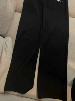 Svarta Nike Air byxor - Säljer ett par svarta byxor i träningsmaterial från Nike Air med broderad logga på vänster sida. Byxorna har raka ben och dragkedja i midjan. Tillverkade i ett mjukt och stretchigt material som känns skönt mot huden. Perfekta för en avslappnad och sportig stil.