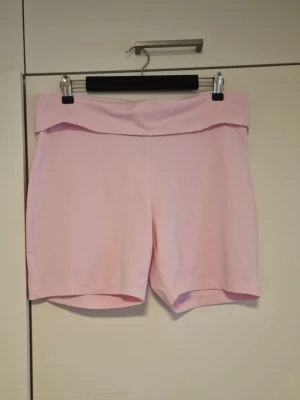 Ljusrosa mjuka shorts i bomull - Säljer ett par ljusrosa shorts med bred, vikt midja. De är tillverkade i mjuk bomull och har en enkel, clean design utan synliga detaljer. Perfekta för varma dagar eller chill hemma.