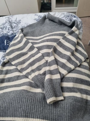 Gråvit randig stickad tröja XL - Mysig stickad tröja från H&M i storlek XL. Tröjan är grå med vita horisontella ränder och har ribbade muddar vid ärmslut, nederkant och hals. Perfekt för kyligare dagar och enkel att matcha med jeans eller kjol.