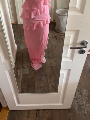 Rosa långklänning med volanger - Snygg rosa långklänning med tunna axelband och flera lager volanger. Klänningen har v-ringning och är tillverkad i ett lätt, flowy material som ger en romantisk känsla. Användes som balklänning och är uppsydd i benen och passar nu mig som är ca 160💕