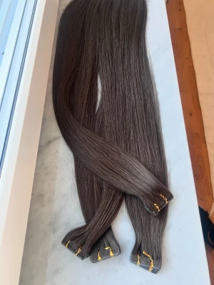 Tape extensions -Slaviskt  - 150 gram av slaviskt löshår i super double drawn vilket innebär extra tjocka toppar i 60 cm.Håret är mörk brunt -mer kallare i verkligheten.Det här är invisible tape (hårstrån hela vägen upp vid fästen) som gör att fästena är osynliga så man kan omöjligt veta att man har i löshår.Jag säljer här på vinted och är återförsäljare för det fina håret,massa kunder som är nöjda med kvalitén då den har en livslängd på minst 3 år -8 år.Lätt att sköta då det är så naturligt och inga onödiga kemikalier på