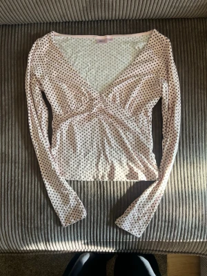 Prickig långärmad topp från Gina Tricot - Supersöt långärmad topp från Gina Tricot i ljusrosa med brun/svarta prickar. Djup v-ringning och figurnära passform, perfekt att styla med jeans eller kjol. Mjukt och stretchigt material för en bekväm känsla.