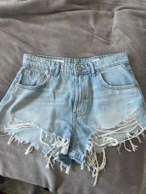 Ljusblå denimshorts med fransar - Säljer dessa super snygga jeans shorts ifrån Zara! Köpte dem förra sommaren, endast använda 2-3 gånger. Super snygga shorts som passar till precis allt! Storlek 38/M. Nypris cirka 380kr, säljes för 150kr