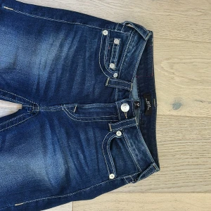 True Religion bootcut jeans - Snygga blå jeans från True Religion med klassisk bootcut och kontrastsömmar. Jeansen har fem fickor, silverfärgade knappar och ikonisk broderad logga på bakfickorna. Materialet är slitstarkt denim med lätt tvättad look och detaljerade sömmar. Dom är använda ett få antal gånger så dom ser nya ut. dom passar mig perfekt som är 170 cm lång. Pris kan diskuteras. Hör gärna av dig om det är nått du undrar över!💗💗(nypris 1 200kr)