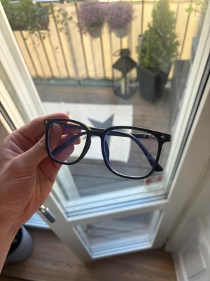 Svarta Chrome H glasögon  - Stilrena glasögon med svart, fyrkantig båge och transparenta linser. Bågarna har små silverdetaljer vid hörnen och en modern vibe som funkar till allt. Tillverkade i plast med klassisk form som ger en clean look.