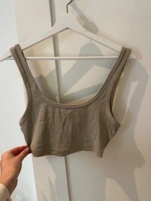 Beige ribbad croppad linnetopp - Säljer en beige ribbad linnetopp med croppad passform. Toppen är ärmlös och har breda axelband samt rundad urringning både fram och bak.