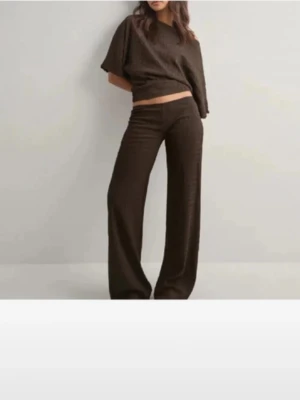 SÖKER I HELST XXS BRUNT/SVART - Mysigt loungewear-set i mörkbrunt från Nelly. Setet består av en kortärmad topp med lös passform och ett par vida byxor med hög midja. Perfekt för chill dagar hemma. Materialet ser ut att vara mjukt och stretchigt för extra komfort .