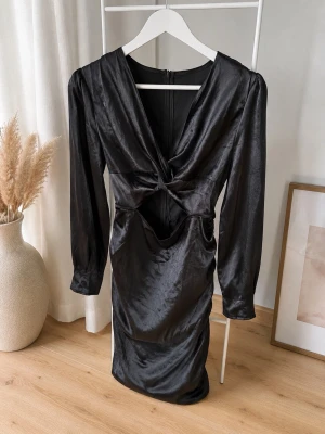 Svart satin klänning med cut out - Snygg svart kortklänning i satin med långärmad design och trendig cut out-detalj framtill. Klänningen har draperad effekt baktill och en djup v-ringning. Perfekt för dig som vill sticka ut med en elegant och modern look.