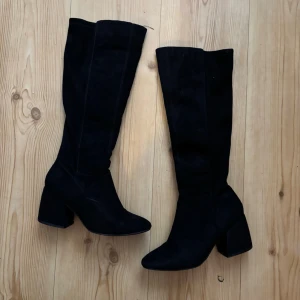 Svarta knähöga stövlar - Säljer ett par svarta knähöga stövlar med bred klack! Stövlarna har dragkedja på insidan och är gjorda i mockaimitation som ger en snygg och stilren look. Defekt: se tre sista bilderna!