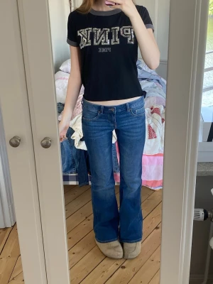 Blå bootcut jeans med låg midja - Säljer ett par klassiska blå bootcut jeans med låg midja och femficksmodell. Jeansen har en snygg tvätt och utsvängda ben, perfekta till sneakers eller boots. Materialet är denim i bomull och de har en tidlös look som passar till det mesta.