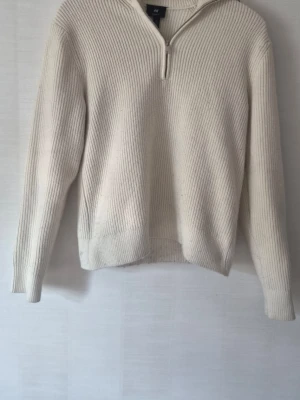 Vit stickad tröja med halv dragkedja H&M - Säljer en stilren vit stickad tröja från H&M med halv dragkedja framtill. Tröjan har ribbstickad struktur, lång ärm och hög krage som kan vikas ner. Perfekt för lager på lager och enkel att matcha till olika outfits.