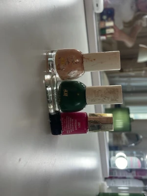 Nagellack i beige, grön och rosa - Säljer tre nagellack: ett beige och ett mörkgrönt från H&M med vita korkar, samt ett knallrosa Revlon 261 Fresh med guldfärgad kork. Perfekt för dig som vill variera mellan neutrala och färgstarka naglar. Alla flaskor är i glas och har klassisk rund form.