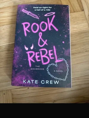 Rook & Rebel av Kate Crew - Säljer boken 'Rook & Rebel' av Kate Crew. Omslaget är svart med lila och rosa detaljer, inklusive en kniv, ett hjärta av kedja och grafiska effekter. Romanen handlar om hämnd, kärlek och motorcykelgäng. Perfekt för dig som gillar spännande och romantisk skönlitteratur.