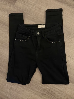 Svarta jeans med nitar från Nina Carter - Snygga svarta jeans från Nina Carter med silverfärgade nitar längs fickorna framtill. Jeansen har klassisk femficksmodell och är tillverkade i stretchigt denimtyg för en bekväm passform. 