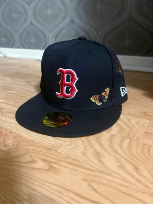 Svart Boston Red Sox keps med broderier - Snygg svart keps från New Era med Boston Red Sox-logga i rött och vitt framtill. Kepsen har broderade fjärilar och bin på sidan för en unik look. Flat skärm och klassisk 59Fifty-modell. Perfekt för dig som vill sticka ut med din stil. Helt ny. Aldrig använt. Storlek 7/ 55.8cm Nypris: 550kr