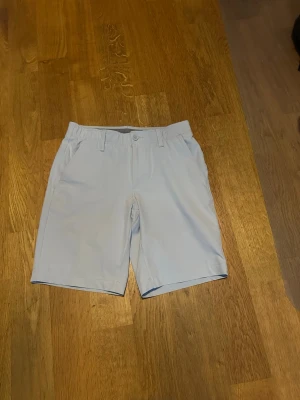Ljusgrå golfshorts från Under Armour - Snygga ljusgrå shorts från Under Armour i storlek 30 som går att använda både till golf men även i vardagen. Shortsen är använda max 5 gånger, och skicket är 9,5/10. Byxorna är som storlek S-M ungefär och materialet är stretchigt