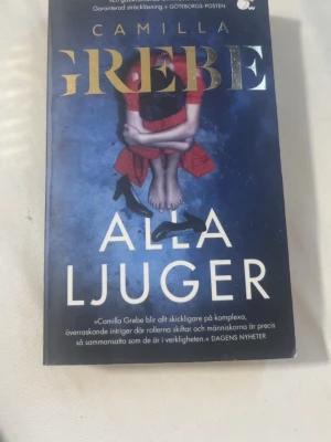 Alla ljuger av Camilla Grebe - En spännande kriminalroman av Camilla Grebe med blått omslag och guldtext. Boken handlar om familjehemligheter och mord, och är en fristående fortsättning på tidigare succéer. Perfekt för dig som gillar psykologiska thrillers och nordisk krim.