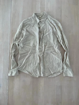 Beige linneskjorta med knappar - Stilren beige skjorta i linne med klassisk krage och knäppning framtill. Skjortan har långa ärmar och en avslappnad passform, perfekt för en enkel och fräsch look. Passar till både jeans och chinos.