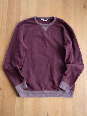 Vinröd sweatshirt från Lee - Säljer en vinröd sweatshirt från Lee med kontrasterande muddar i grått vid hals, ärmslut och nederkant. Tröjan har rund halsringning och klassisk relaxed passform. Perfekt för en avslappnad och stilren look.