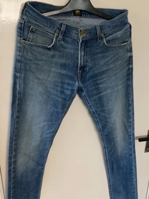 Blå slim fit jeans från Lee - Säljer ett par blå slim fit jeans från Lee med klassisk femficksmodell och snygg slitning på framsidan. Jeansen har normal midja, dragkedjegylf och Lee-lapp bak i midjan. Perfekta till en avslappnad och trendig stil.