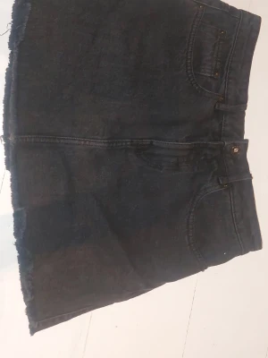 Svart jeanskjol med rå kant - Säljer en jätte fin svart jeanskjol. Kjolen har knapp och dragkedja framtill och är i en kort modell. Säljer då den tyvärr är för liten för mig. 