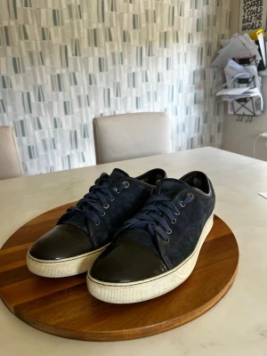 Lanvin Cap toe - Snygga blå sneakers från Lanvin med mörkblå mocka och svarta lackdetaljer på tån. Väldigt bra skick förutom ett par skavanker inne i skon, men de är inget som syns utifrån eller märks vid användning enligt mig. Rekommenderar att man knyter skorna själv. Storlek 42,5. Skriv vid frågor 