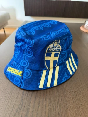 Sverige Fiskehatt Buckethat Solhatt Landslaget - Handgjord fiskehatt tillverkad av en Sverige-landslagströja. Hatten är sydd i one size-modell. Jag skulle dock säga att den är lite mindre än en vanlig one size modell, har du ett stort huvud så blir det svårt.  