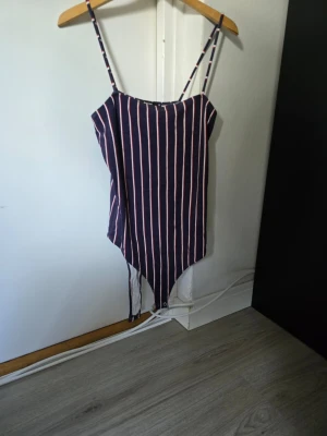 Randig body med smala axelband från bikbok - Säljer en body med marinblå bas och vita vertikala ränder. Modellen har smala axelband och knäppning i grenen. Materialet känns mjukt och stretchigt, perfekt för en bekväm och snygg look.