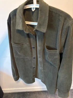 Olivgrön overshirt i manchester - Säljer en knappt använd olivgrön overshirt i mjuk manchester med två stora bröstfickor och knäppning framtill. Skjortjackan har klassisk krage och raka ärmar, perfekt för lager på lager. Snygg och enkel att styla till olika outfits. Passar L och M.