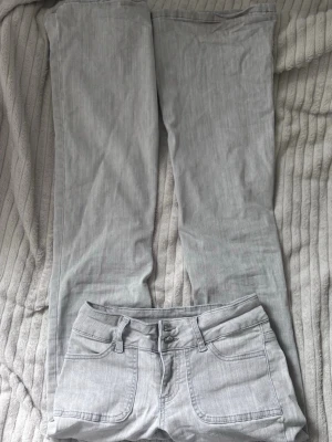 Lowwaist jeans Nelly - Ett par ljusgråa lågmidjade jeans från Nelly med detaljerade fickor på framsidan. Storlek 32 och passar mig bra som är 159cm ungefär. De har lite skavanker i form av lite uppnött typ längst ner. Dock är det inget som syns mycket. Har använts ett par gånger innan de blev för små.