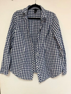 Blårutig skjorta med knappar - Klassisk blårutig skjorta med långa ärmar och knappar framtill. Skjortan har en avslappnad passform och är tillverkad i mjuk bomull, perfekt för en chill och stilren look. Passar lika bra till jeans som till chinos. ( tänk på jag har hund i hemmet) 