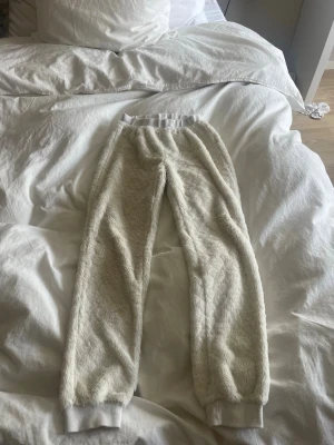Vita fluffiga mjukisbyxor - Supermysiga vita mjukisbyxor med fluffig, teddy-liknande yta. Byxorna har resår i midjan och vid bensluten för extra komfort och en avslappnad look. Perfekta för chill dagar hemma eller när du vill vara extra bekväm. Inget synligt märke.