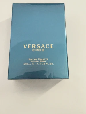 Versace Eros Eau de Toilette 100 ml - Versace Eros Eau de Toilette i en lyxig, blågrön glasflaska med Medusa-huvud i relief och guldfärgade detaljer. Flaskan rymmer 100 ml och har en elegant, fyrkantig form. Kommer i en matchande blå kartong med guldfärgad text.