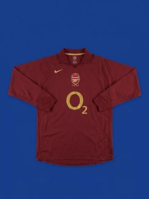 Arsenal Highbury tröja vinröd Nike - Vinröd långärmad Arsenal Highbury 1913-2006 tröja från Nike med guldfärgade detaljer och O2-logga på bröstet. Broderat Arsenal-emblem och klassisk krage. Perfekt för fotbollsfans som vill sticka ut på läktaren.