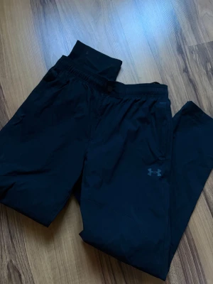  Under Armour Raka Byxor - Säljer ett par svarta mjukisbyxor från Under Armour med diskret logga på benet. Byxorna har resår i midjan och raka ben, perfekta för chill eller träning. Materialet känns lätt och smidigt, vilket gör dem riktigt bekväma att ha på sig. Använda två gånger. 