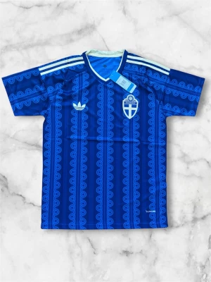 Blå Sverige fotbollströja Adidas - Säljer en blå fotbollströja från Adidas med Sveriges landslagsemblem på bröstet. Tröjan har ett mönster i olika blå nyanser, vita Adidas-ränder på axlarna och vit V-ringad krage. Tillverkad i lätt och funktionellt material, perfekt för träning eller match.