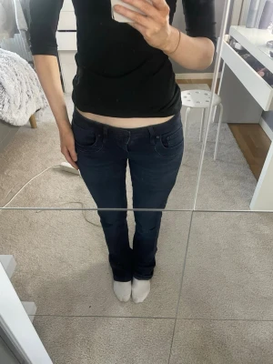 Mörkblå bootcut jeans - Säljer ett par mörkblå bootcut jeans med låg midja och klassisk femficksdesign. Jeansen har en smal passform över låren och lätt utsvängda ben. Perfekta till en avslappnad och trendig look.