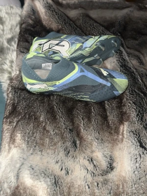 Puma Future Z blå/gula fotbollsskor - Säljer ett par Puma Future Z fotbollsskor i blått, gult och svart med coolt mönster och stora Puma-loggor. Skorna har en strumpliknande passform och greppvänlig sula för spel på gräs. Perfekta för dig som vill sticka ut på planen!