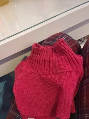 Rosa stickad halskrage och en färglagd mössa - Säljer en rosa stickad halskrage med polokrage. Perfekt att dra över huvudet för extra värme under jackan. Mjuk och stretchig i materialet, enkel att matcha med olika outfits. Inget synligt märke. Till följer en färgglad mössa som kan värma öronen.