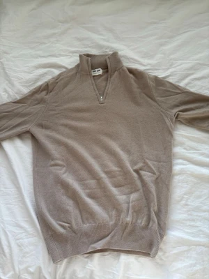 Soft goat ziptröja beige Strlk: M - Beige stickad tröja från SOFT GOAT med halvzip och ståkrage. Tröjan är i M men passar absolut en storlek S också. Perfekt för lager-på-lager och enkel att matcha med jeans eller chinos. 