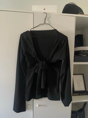 Svart omlottopp med knyt - Trendig svart omlottopp med långa ärmar och snygg knytning framtill. Djup v-ringning, stretchig och skön material. 