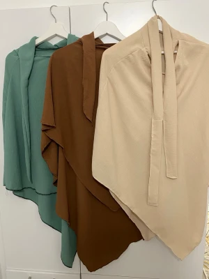 Tre st khimar  i grönt, brunt och beige - Säljer tre snygga khimar i olika färger: en i dämpad grön, en i varm brun och en i ljus beige. Alla har asymmetrisk form och långa band att knyta med. Perfekta att slänga över axlarna för en cool och avslappnad look. Helt oanvända, köpta utomlands