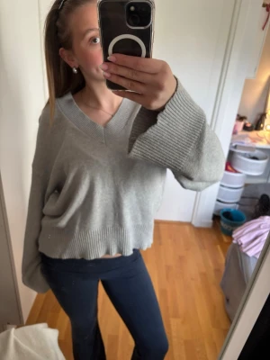 Grå stickad tröja Gina Tricot🫶🏻 - Grå stickad tröja från Gina Tricot med croppad passform och djup V-ringning. Tröjan har breda ribbade muddar vid ärmslut och nederkant samt långa ärmar. Perfekt för en avslappnad och trendig look. Superskön!!🤍