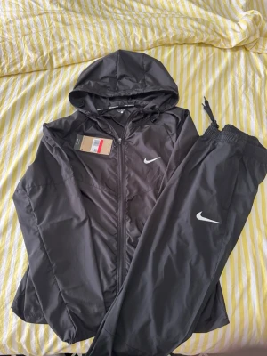 Nike Miller tracksuit  - Hej jag säljer En fin lätt tränings tracksuit från Nike sportswear i modellen Miller i de klassiska färgen svart  perfekt för träning och att bara ha som en bekväm skön outfit den är helt ny faktiskt bara testats på men satt inte så bra som jag ville tyvärr 😊