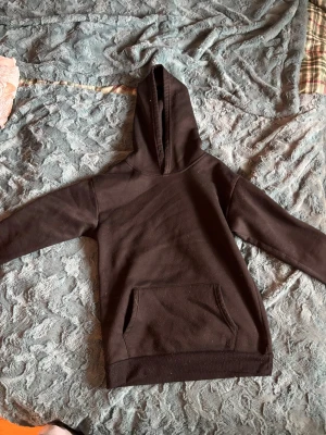 Svart hoodie med tryck och ficka - Svart hoodie med stor känguruficka framtill och huva. På ryggen finns ett coolt tryck med foton och texten 'BE TRUE OF'. Hoodien har en avslappnad passform och är gjord i mjukt bomullsmaterial, perfekt för en chill look.