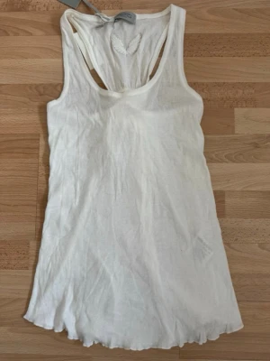 Ny, Hunkydory vit linnetopp från FunkyTown Essentials - Säljer en vit ärmlös linnetopp från Hunkydory . Toppen har rund halsringning, snygg knytning i ryggen och lätt vågig nederkant. Perfekt till sommarens alla outfits och superenkel att styla med andra plagg. Ordpris 699kr, nu 299kr. Bomull 100%