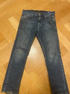 Mörkblå slim fit jeans från Replay - Mörkblå slim fit jeans från Replay med klassisk femficksdesign och lätt slitna detaljer. Jeansen har normal midja och raka ben, tillverkade i stretchigt denim för en bekväm passform. Perfekta till sneakers eller boots.